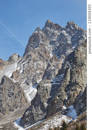 rugged mountain peak under blue sky, jagged edges, snow, high-altitude location 119008305