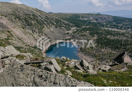 A blue green mountain lake surrounded by stone hills with steep slopes, huge stones and coniferous forest 119008348