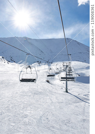 Ski lift with empty chairs at winter resort. Sunny day, blue sky. Mountain slope 119008361