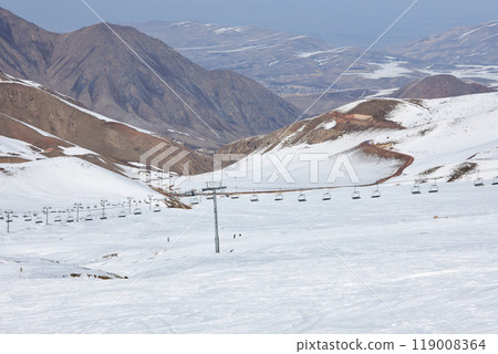 Cable car at winter ski resort. Snowy slope of ski track and snowless southern slopes of high mountains 119008364