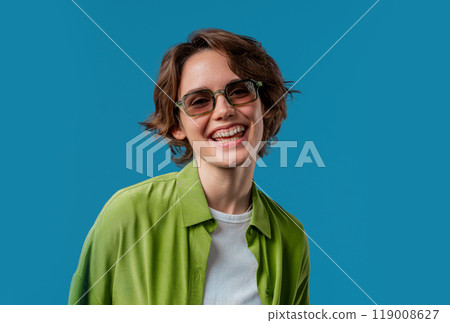 Smiling woman in dark green glasses. Positive stylish lady. Eyewear, sunglasses, fashion accessories. Blue studio background 119008627