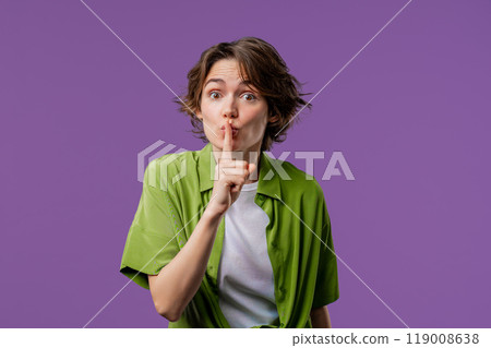 Beautiful stylish woman holding finger on lips, violet studio background. Pretty lady with gesture of shhh, secret, silence, conspiracy, gossip, rumors concept. Beautiful stylish woman holding finger on lips, violet studio background. Pretty lady with gesture of shhh, secret, silence, conspiracy, gossip, rumors concept. 119008638