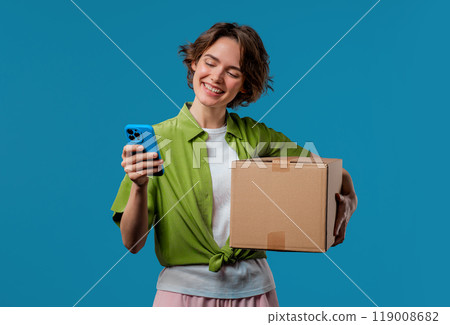 Excited smiling woman, online shopping consumer received cardboard order parcel box, desired purchase. Mobile phone, smartphone mockup with copy space screen for your advertisement 119008682