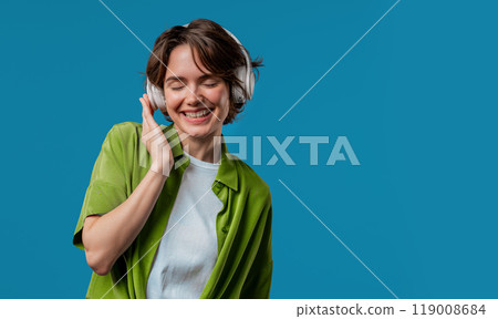 Happy woman gets high, listening music, enjoying dance with headphones on Blue studio backdrop. Copy space. Radio, wireless modern sound technology, online player Happy woman gets high, listening music, enjoying dance with headphones on Blue studio backdrop. Copy space. Radio, wireless modern sound technology, online player 119008684