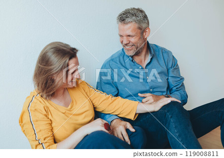 A happy couple is having fun at home while sitting on the floor. A happy couple is having fun at home while sitting on the floor. 119008811