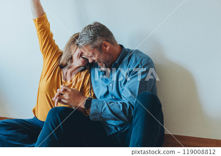 A happy couple is having fun at home while sitting on the floor. A happy couple is having fun at home while sitting on the floor. 119008812