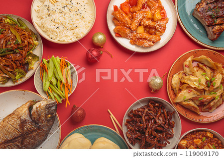 Chinese new year festive table with traditional dishes top view on red background: kung pal chicken, sweet and sour pork, noodles, dumplings, mapo tofu, fish, rice, fortune cookies. Copy space Chinese new year festive table with traditional dishes top view on red background: kung pal chicken, sweet and sour pork, noodles, dumplings, mapo tofu, fish, rice, fortune cookies. Copy space 119009170
