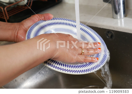 Washing dishes, plates, and utensils under running water in the kitchen sink area Washing dishes, plates, and utensils under running water in the kitchen sink area 119009383