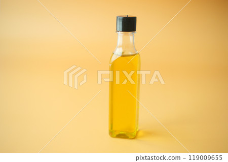A Clear Glass Bottle filled with Cooking Oil set against a Bright Yellow Background 119009655