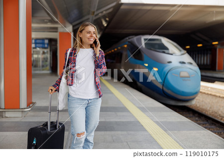 A traveler with luggage stands at a busy train station, soaking in the atmosphere of adventure 119010175