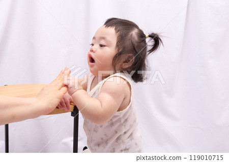 [Baby with twin tails standing up holding onto a table] 119010715