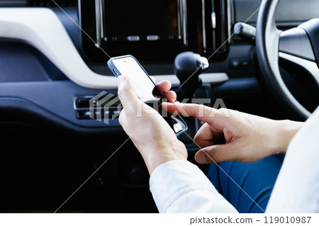 A man in work clothes operating a smartphone in a car 119010987