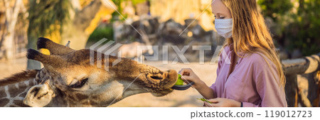 BANNER, LONG FORMAT Happy young woman watching and feeding giraffe in zoo wearing a medical mask during COVID-19 coronavirus. Happy young woman having fun with animals safari park on warm summer day BANNER, LONG FORMAT Happy young woman watching and feeding giraffe in zoo wearing a medical mask during COVID-19 coronavirus. Happy young woman having fun with animals safari park on warm summer day 119012723