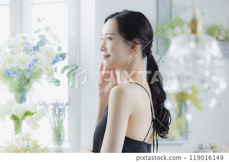 A woman in a black camisole dress standing by the window 119016149