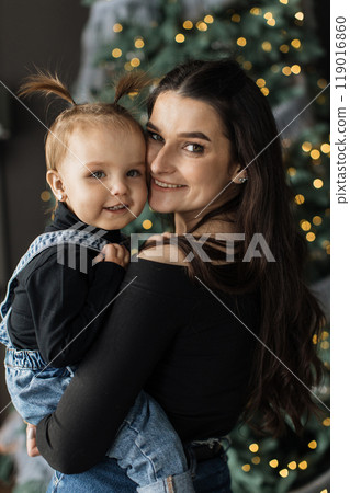 Mother and daughter smiling by Christmas tree at home 119016860