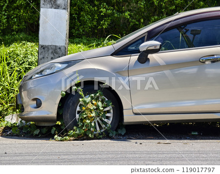A silver car that has a broken tire and is covered with leaves 119017797