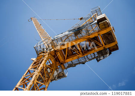 A large yellow crane stands out against a bright blue sky 119017881
