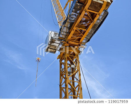 A large yellow crane stands out against a bright blue sky 119017959