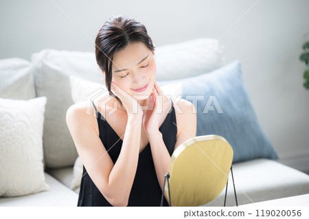 A woman with beautiful bare skin who does skin care while looking in the mirror, eyes closed 119020056