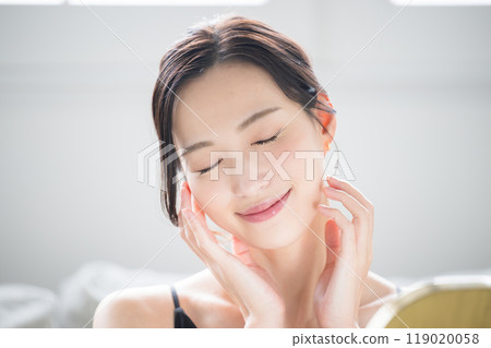 Close-up of a woman with beautiful bare skin who does skin care while looking in the mirror, eyes closed Close-up of a woman with beautiful bare skin who does skin care while looking in the mirror, eyes closed 119020058