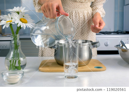 Woman pouring half of water glass to pan cooking on kitchen at home. 119020561