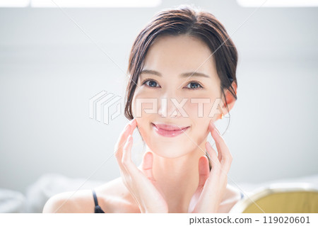 Close-up of woman touching her beautiful skin with both hands, concerned about dry cheeks and skin care, looking at camera 119020601