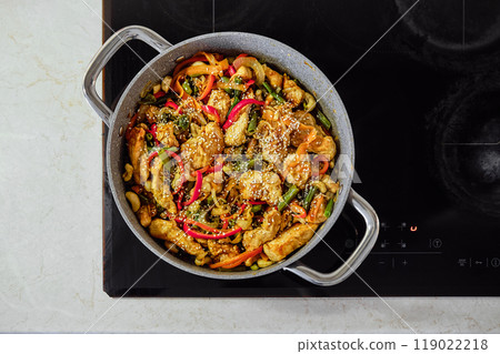 Stir-fried chicken with vegetables and cashews on an induction cooktop in a kitchen setting Stir-fried chicken with vegetables and cashews on an induction cooktop in a kitchen setting 119022218