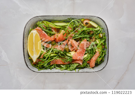 Fresh arugula salad topped with salmon and lemon on a white marble countertop 119022223