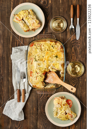 Delicious vegetable casserole served on plates with wine and utensils on a wooden table 119022236