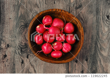 Freshly harvested radishes in a rustic wooden bowl on a weathered wooden surface 119022245