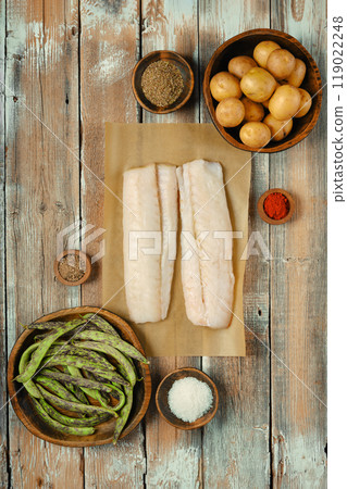 Fresh cod fish fillets with assorted vegetables and spices on a rustic wooden table in a kitchen 119022248