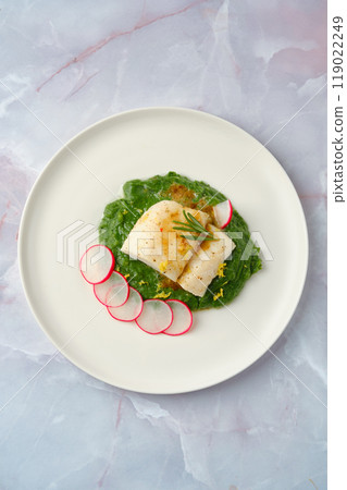 Elegant white cod fish served on vibrant spinach puree with sliced radishes, garnished for visual appeal 119022249