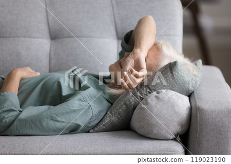 Older woman lying on sofa, feeling fatigued, unmotivated, taking rest Older woman lying on sofa, feeling fatigued, unmotivated, taking rest 119023190