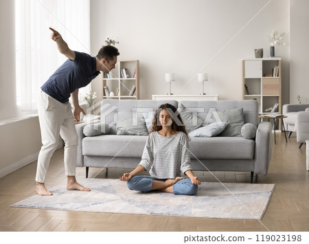 Annoyed frustrated husband shouting at ignoring meditating wife 119023198