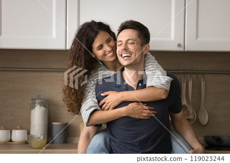 Happy joyful husband piggybacking pretty Latin wife, carrying in arms Happy joyful husband piggybacking pretty Latin wife, carrying in arms 119023244