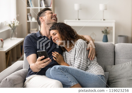Cheerful young husband and wife in love relaxing with smartphone Cheerful young husband and wife in love relaxing with smartphone 119023256