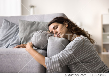 Tired depressed young woman sleeping on floor, embracing couch Tired depressed young woman sleeping on floor, embracing couch 119023402