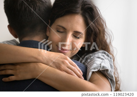 Peaceful pretty Latin wife embracing husbands neck with closed eyes, 119023420
