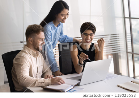 Three cheerful multiethnic business colleagues using laptop together 119023558