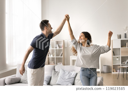 Cheerful carefree married couple dancing at home, holding hands 119023585