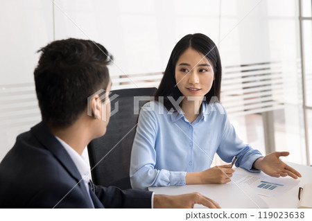 Positive young Asian businesswoman talking to male colleague at meeting Positive young Asian businesswoman talking to male colleague at meeting 119023638