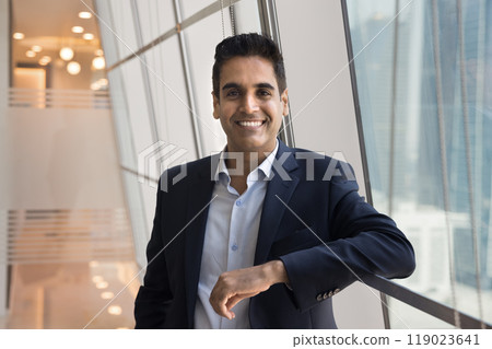 Happy successful Indian businessman leaning on rail at window 119023641