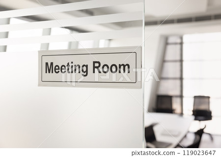 Meeting room sign on office glass wall with empty workspace 119023647