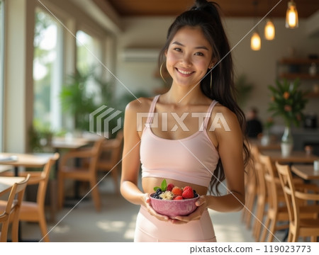 Smiling young woman holding a bowl of fresh fruit in an open-air caf?, radiating a healthy and vibrant lifestyle Smiling young woman holding a bowl of fresh fruit in an open-air caf?, radiating a healthy and vibrant lifestyle 119023773