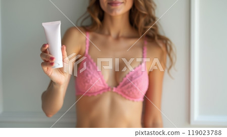 Model in pink lace bikini holding a white sunscreen tube, promoting skincare and sun protection in a fresh, beachy vibe 119023788