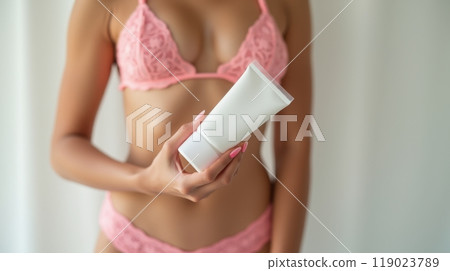Model in pink lace bikini holding a white sunscreen tube, promoting skincare and sun protection in a fresh, beachy vibe 119023789