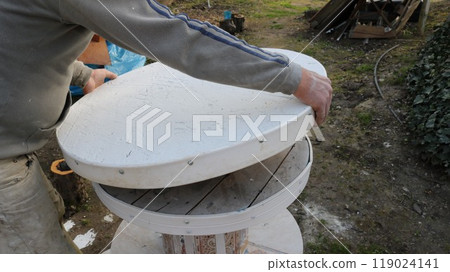 craftsman holding heavy round table top and installing it on thick base, assembling homemade table from white material outdoors, installation of round tabletop by carpenter or assembler craftsman holding heavy round table top and installing it on thick base, assembling homemade table from white material outdoors, installation of round tabletop by carpenter or assembler 119024141