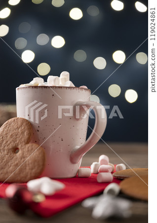 Cup of hot chocolate decorated with tiny marshmallows with a big cookie leaning on the mug 119024861