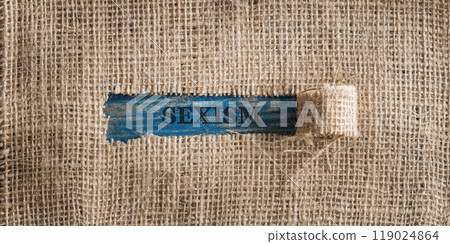 Linen fabric with a torn window in the middle with a Sexism sign in it 119024864
