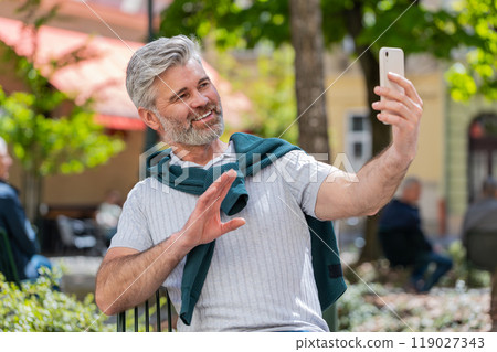 Mature man blogger use smartphone communicating video call online with subscribers recording stories 119027343